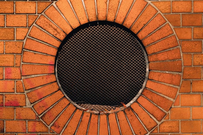A round metal mesh vent set into an exterior brick wall